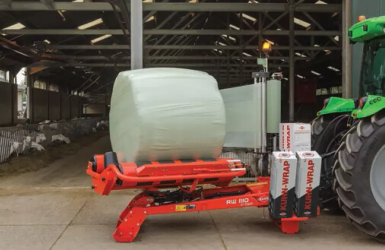 RW 1110 wrapping a round bale in front of a goat barn.
