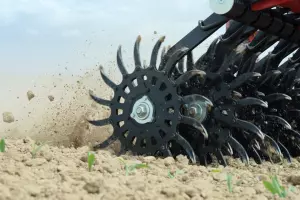 A Rotary hoe Starliner churns through brown soil, kicking up dirt and debris in a farm field.