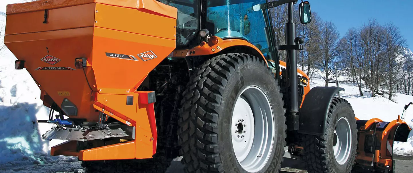 AXEO salt, sand, gravel and fertiliser spreader at work on a mountain road in the snow with a skier