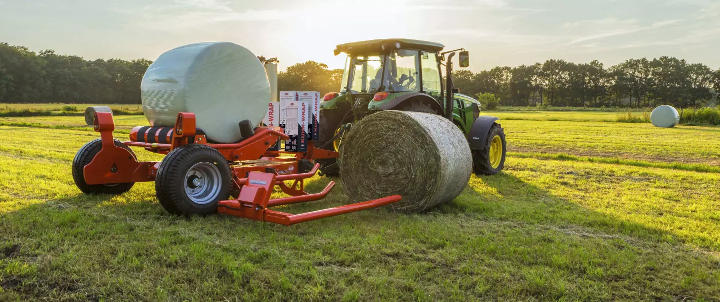 RW 1610 bale trailed round bale wrapper loading a round bale during wrapping of another bale.