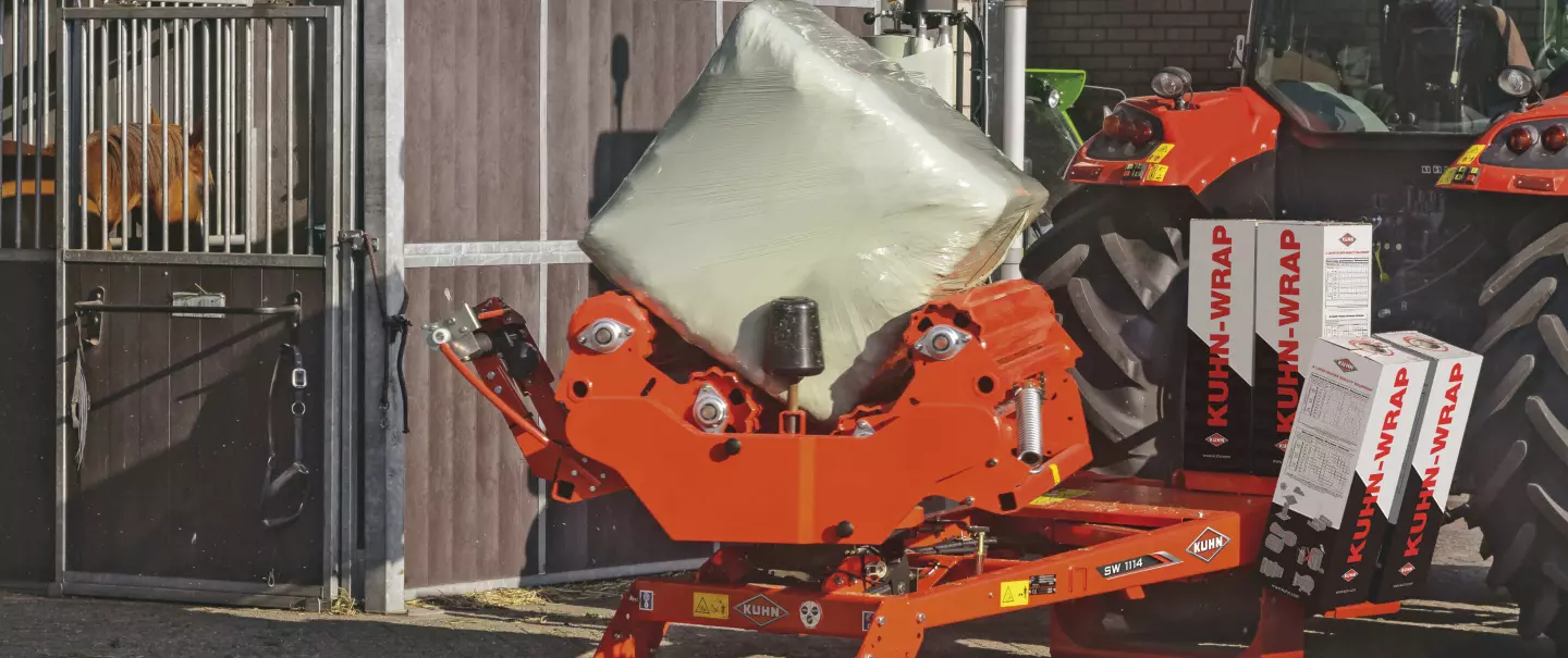 A SW1114 square bale wrapper, wrapping stationairy in front of a horse stable.
