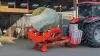 A KUHN SW1114 wrapping a round bale in front of a horse stable.